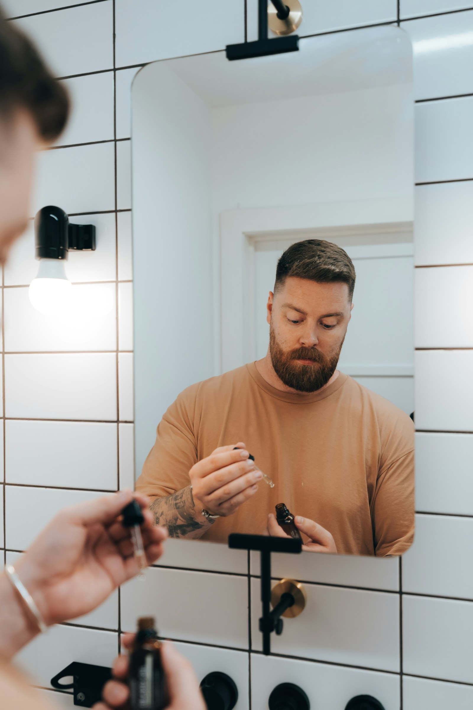 A person applying serum with a dropper in front of a bathroom mirror