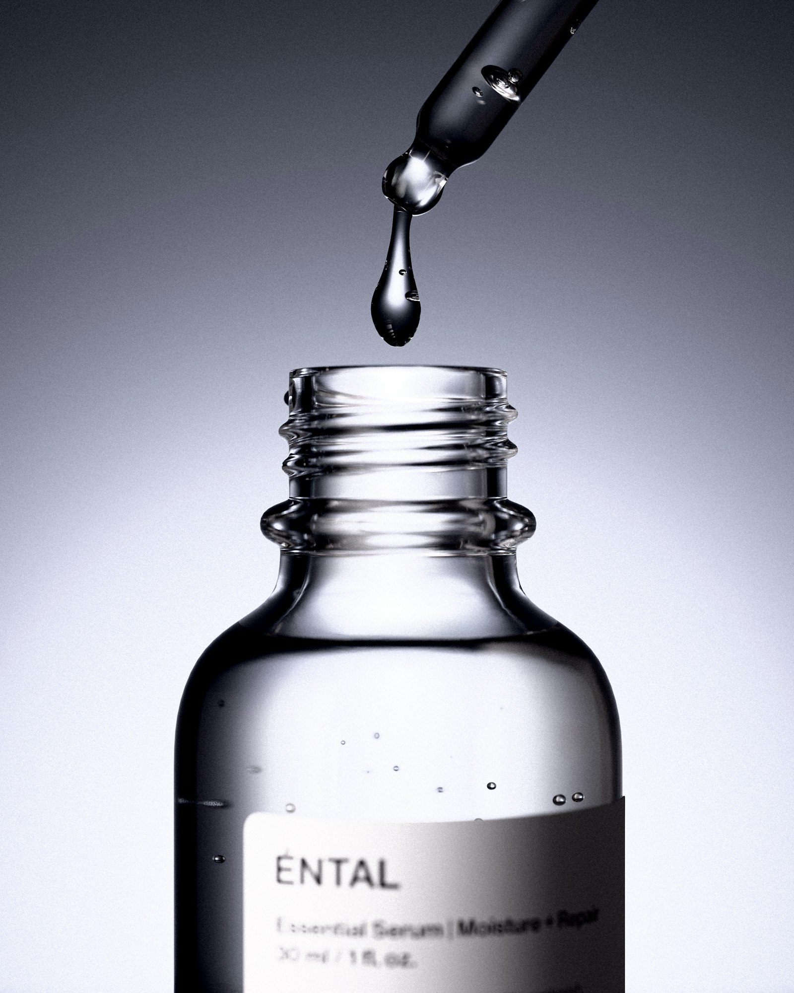 A dropper releasing a drop of clear serum into a glass bottle