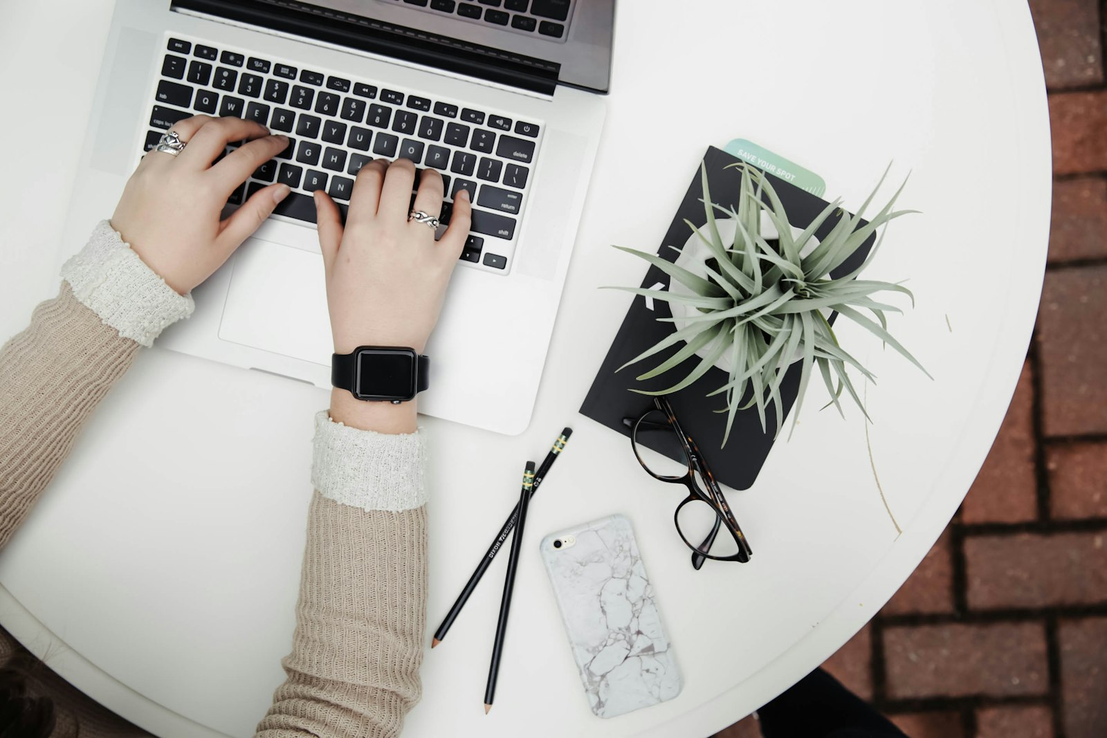 Hands typing on a laptop on a white desk beside a plant