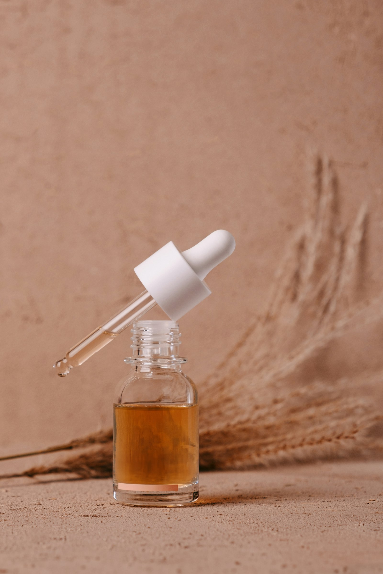 A dropper over a bottle of amber serum on a warm-toned background
