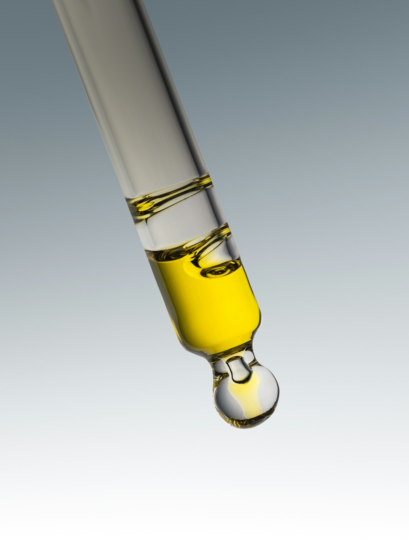 A glass dropper holding a golden serum against a grey background